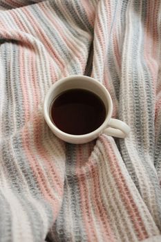 Ceramic mug filled with coffee, nestled on a warm striped blanket, evoking a sense of coziness and relaxation.