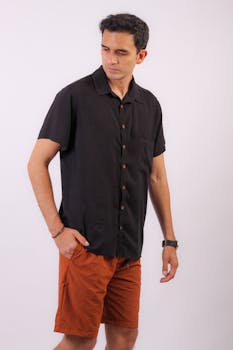 Fashionable man in black shirt and orange shorts posing against a white background.