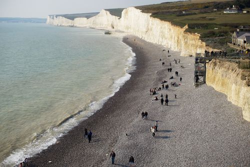 Free Aerial view of Seven Sisters chalk cliffs with people on the pebble beach by the sea. Stock Photo