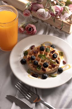 Enjoy a delectable waffle topped with blueberries, raisins, mint, and honey alongside refreshing orange juice.
