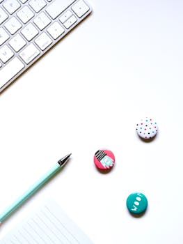 A clean, minimalist workspace featuring a keyboard, pen, and decorative buttons on a white background.