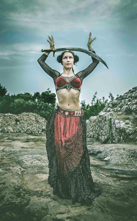 Gratis Wanita Mengenakan Gaun Hitam Dan Merah Memegang Pedang Berdiri Di Permukaan Batu Pada Siang Hari Foto Stok