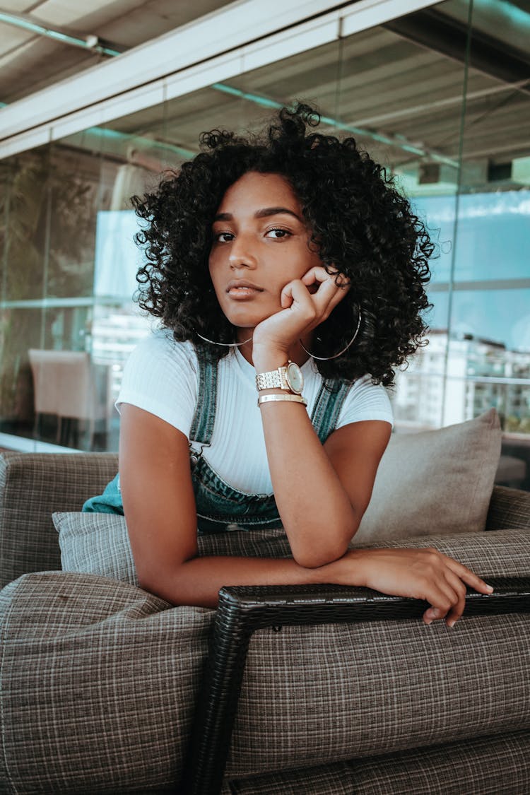 Woman With Curly Black Hair Kneeling On Sofa With Head Propped Up