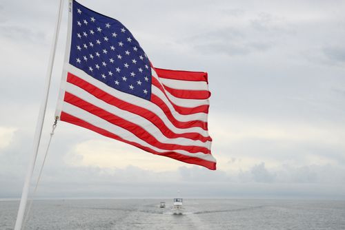 Free A vibrant American flag flutters on a boat with a vast ocean and cloudy sky backdrop. Stock Photo
