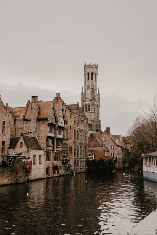 Free Picturesque view of Bruges' historic Belfry overlooking a serene canal with traditional architecture. Stock Photo