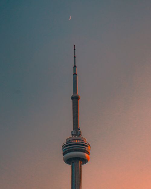 Free Beautiful capture of the CN Tower in Toronto against a moonlit evening sky, reflecting golden hues. Stock Photo