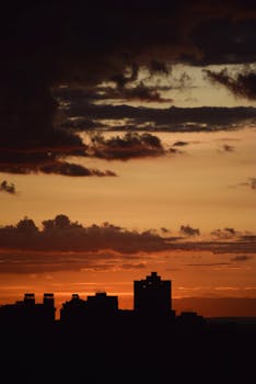 Silhouette of city buildings under a dramatic, golden sunset sky.