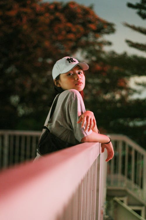 Woman in White Baseball Cap Leaning on Metal Railings