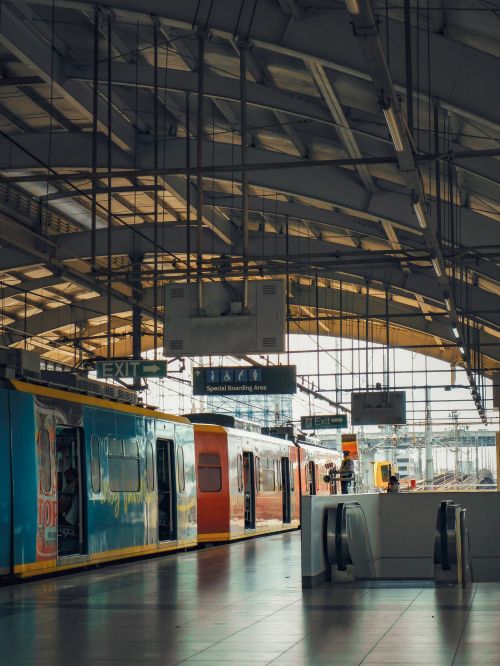 Free Empty railway platform with colorful trains, reflective floors, and high arched roofs. Stock Photo