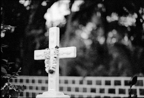 Free A serene black and white photo of a cemetery cross adorned with a floral garland, embracing a somber ambiance. Stock Photo
