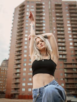 Blonde woman poses confidently in front of a high-rise building in Des Moines, IA, showcasing urban fashion.