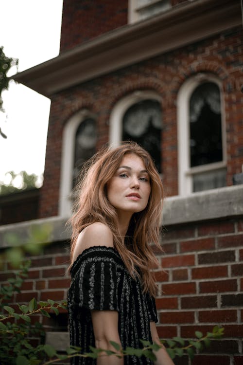 Woman in Off Shoulder Blouse Standing Beside a Brick House