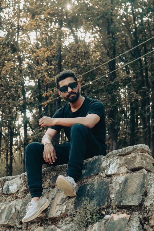 Free Casual portrait of a young man relaxing on a stone wall in a forest area, exuding a relaxed vibe. Stock Photo