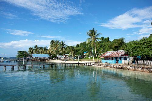 Free Serene island view with a boardwalk and palm trees under a bright blue sky. Stock Photo