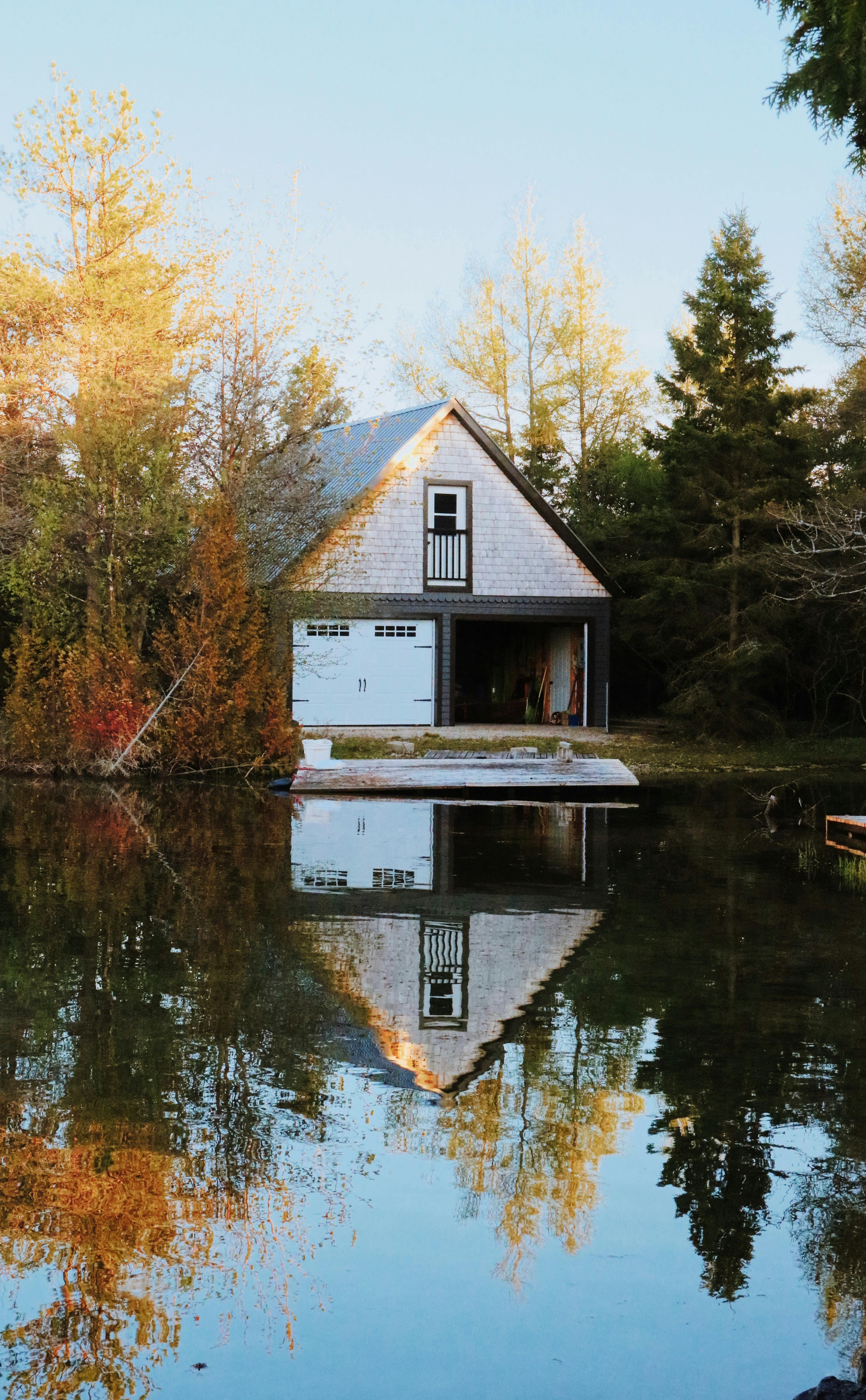 A serene autumn landscape featuring a lakeside cottage reflecting in calm water surrounded by trees.