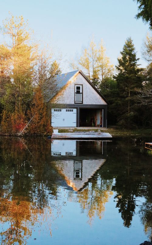 Free A serene autumn landscape featuring a lakeside cottage reflecting in calm water surrounded by trees. Stock Photo