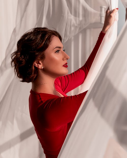 Woman in Red long Sleeves Holding a Curtain