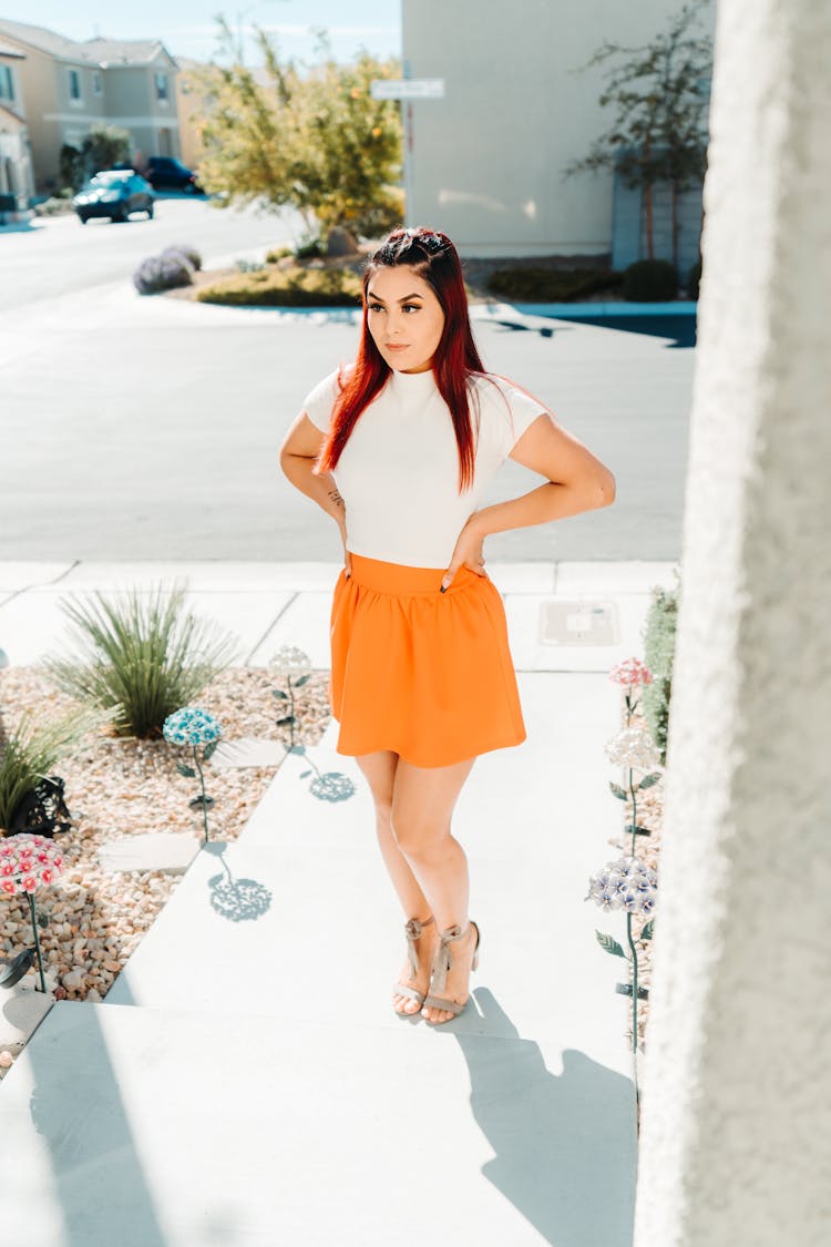 Woman In Orange Skirt Standing By Sidewalk