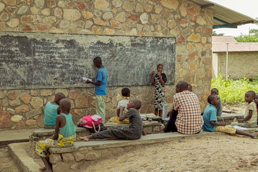 Children studying outdoors with a teacher, engaging with a blackboard at a rural school.
