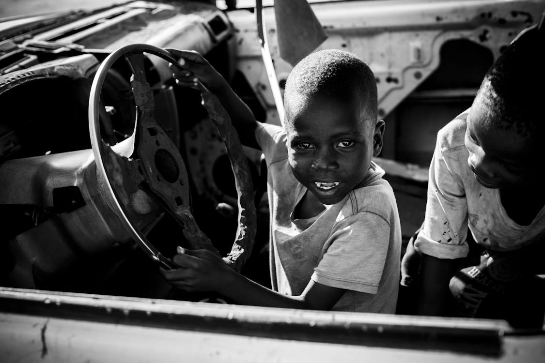 Grayscale Photo Boys Playing on a Broken Car