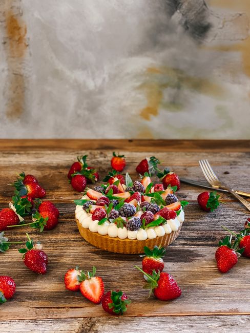 A vibrant strawberry tart surrounded by fresh fruit on a rustic wooden table.
