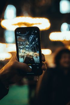A hand holds a smartphone displaying a grand architectural interior with chandeliers.