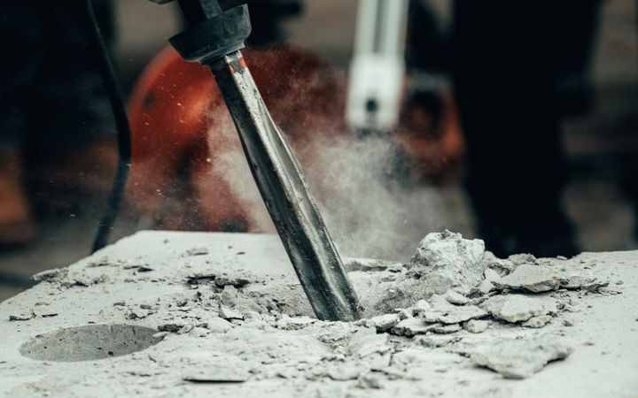 A detailed close-up of a power tool chipping away at a concrete block, capturing action and dust.