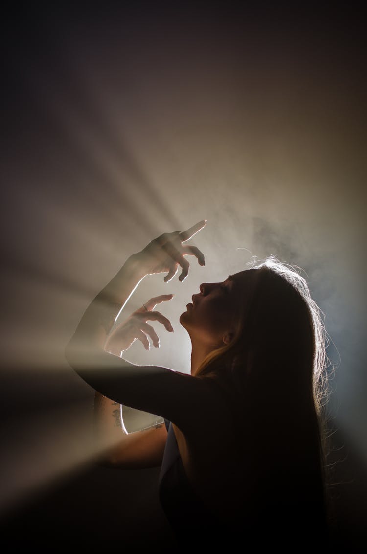 Back Lit Profile Of Woman With Arms Raised