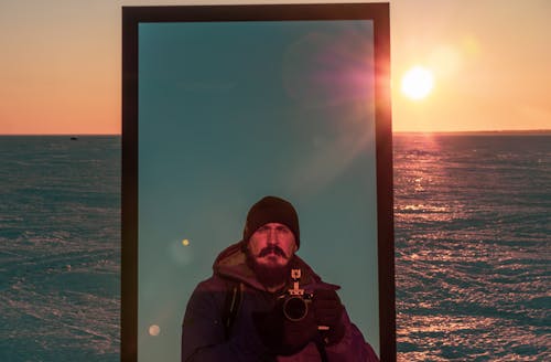 Free A man is reflected in a mirror that stands on the ice of a frozen sea at sunset Stock Photo