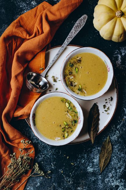 Top view of two bowls of pumpkin soup garnished with herbs and spices, perfect for autumn.