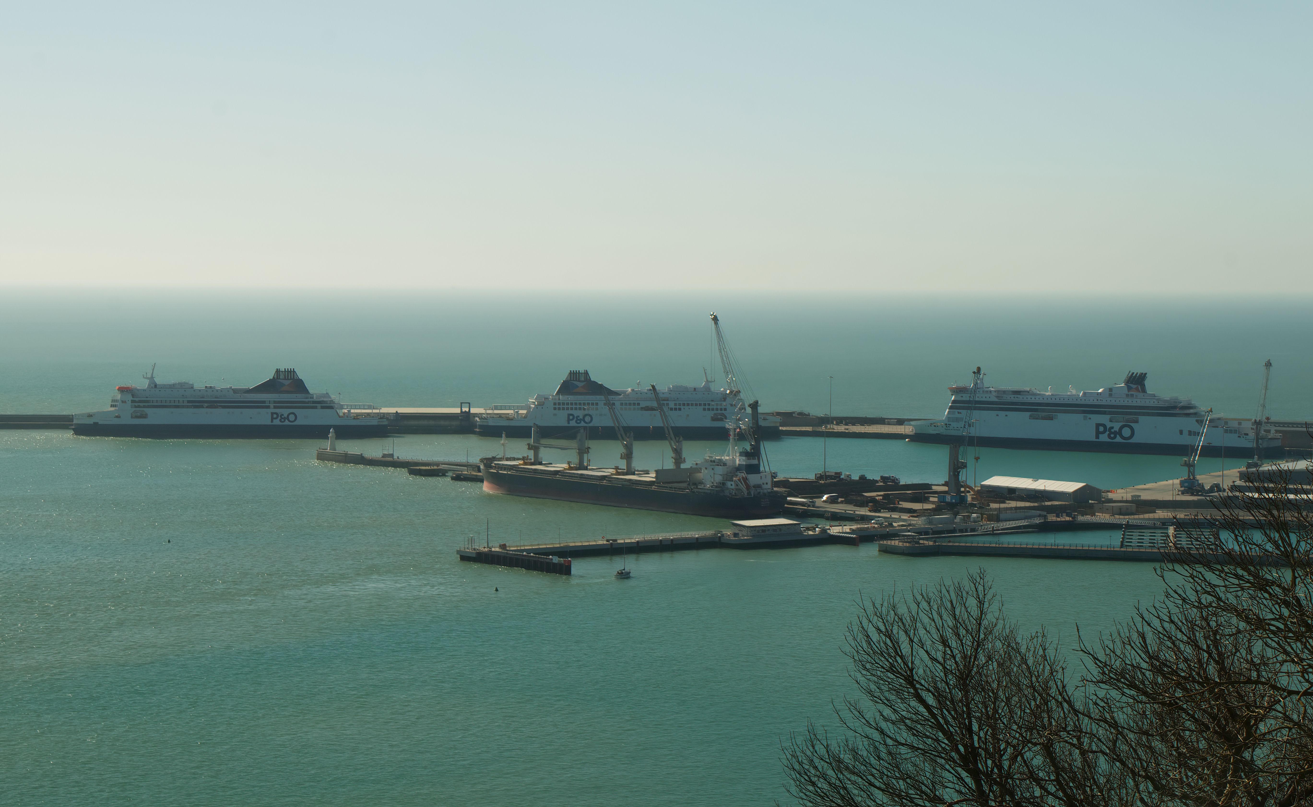 Three P&O ferries docked at a harbour beside cargo cranes and calm sea