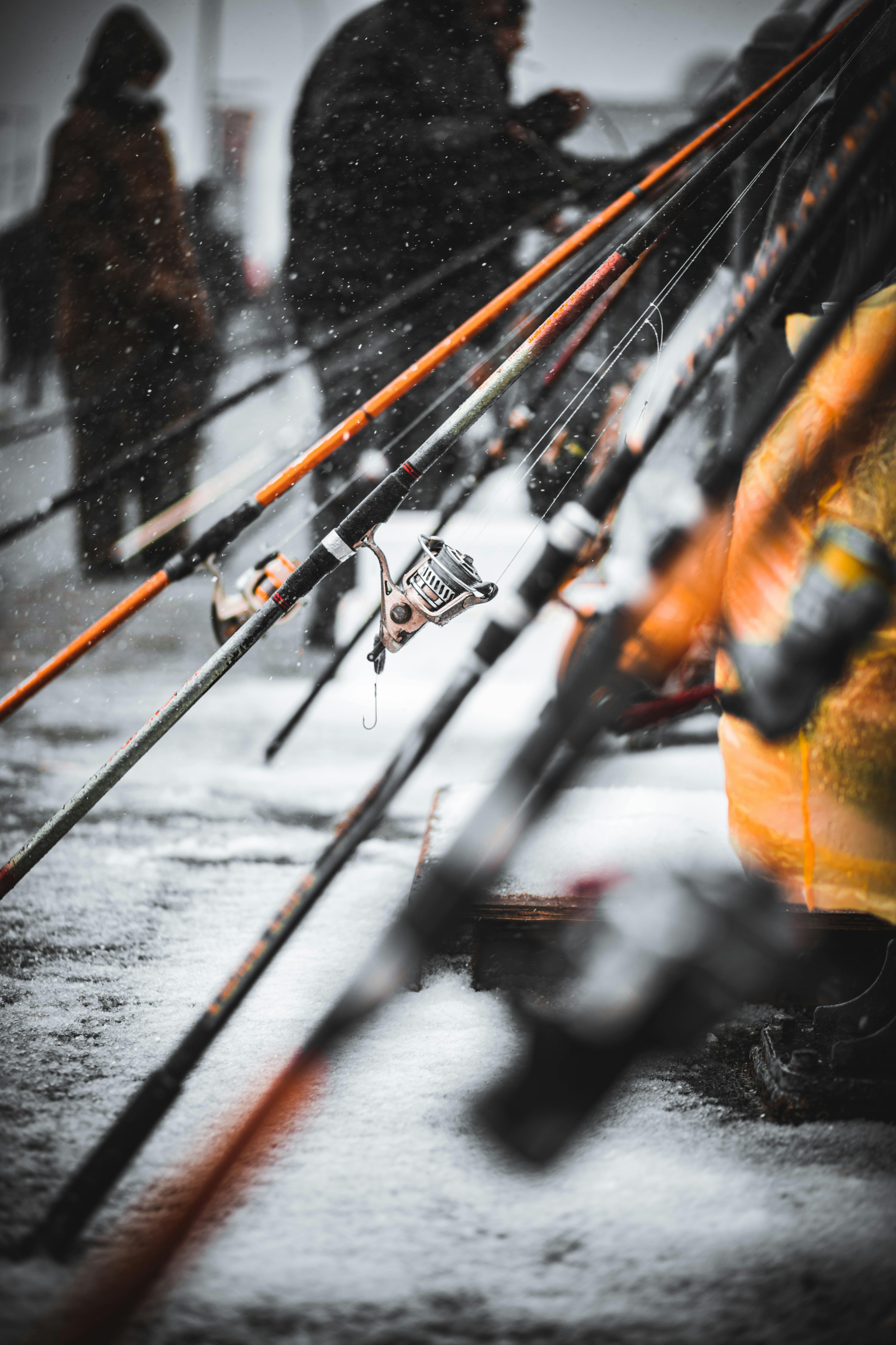 Close-up of fishing rods lined up outdoors in a snowy winter scene with people in the background.