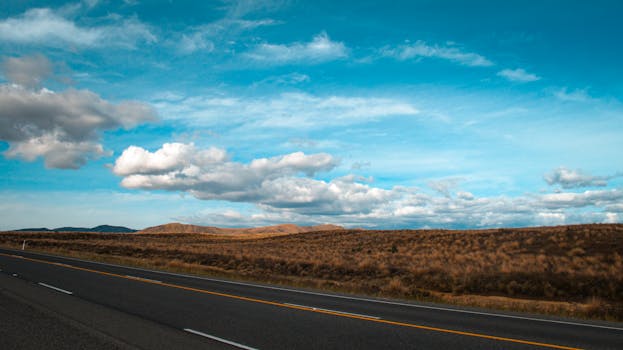 Expansive countryside road with bright blue sky and fluffy clouds, perfect for transportation themes.