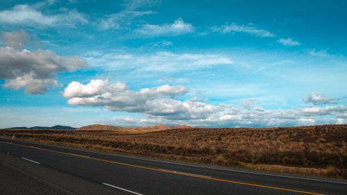 Free Expansive countryside road with bright blue sky and fluffy clouds, perfect for transportation themes. Stock Photo