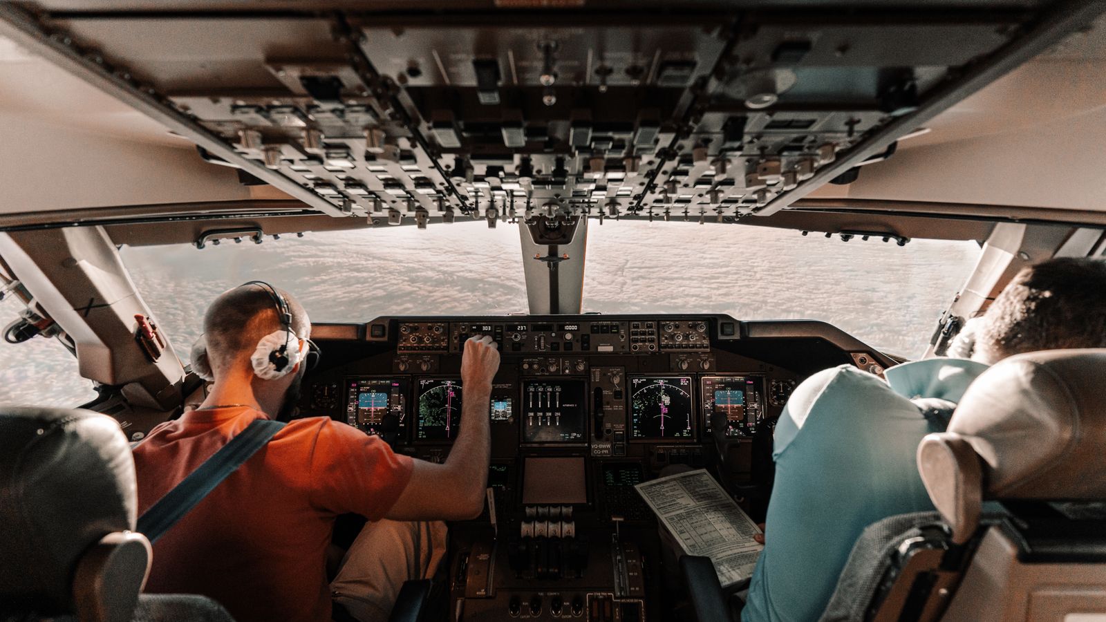 Pilots navigating a commercial plane cockpit with daytime views outside.