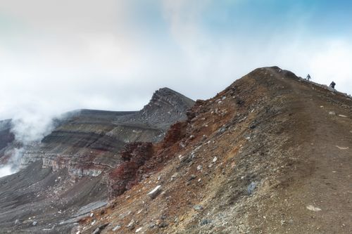 Free Stunning landscape of a volcanic ridge with hikers exploring the terrain under a clear sky. Stock Photo