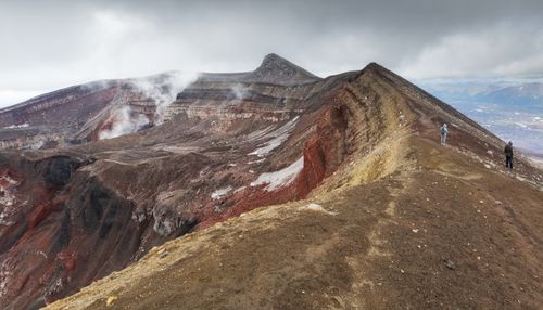 Free Hikers explore a vibrant volcanic ridge with breathtaking mountain views under cloudy skies. Stock Photo