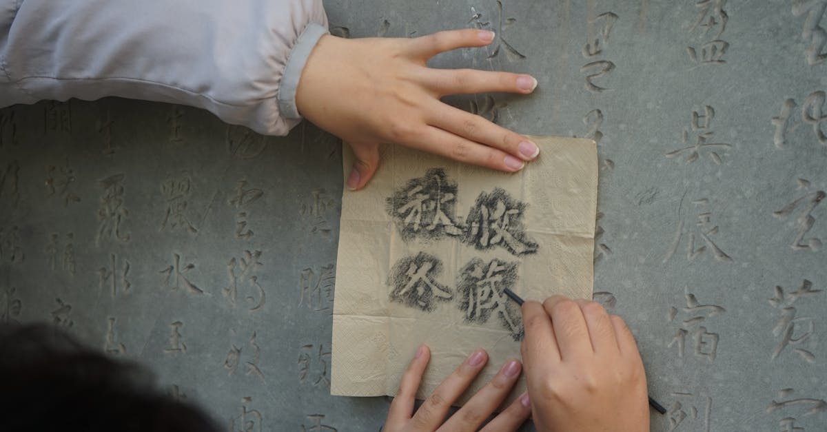Close-up of hands using charcoal to trace Chinese characters on a stone wall, highlighting calligraphy art.