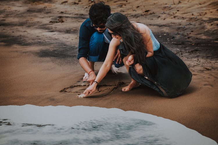 Couple Drawing Heart On Beach