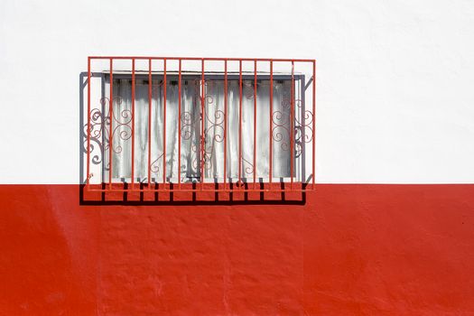 A striking minimalist image of a red and white wall featuring a window with decorative iron grills. Perfect for design concepts.