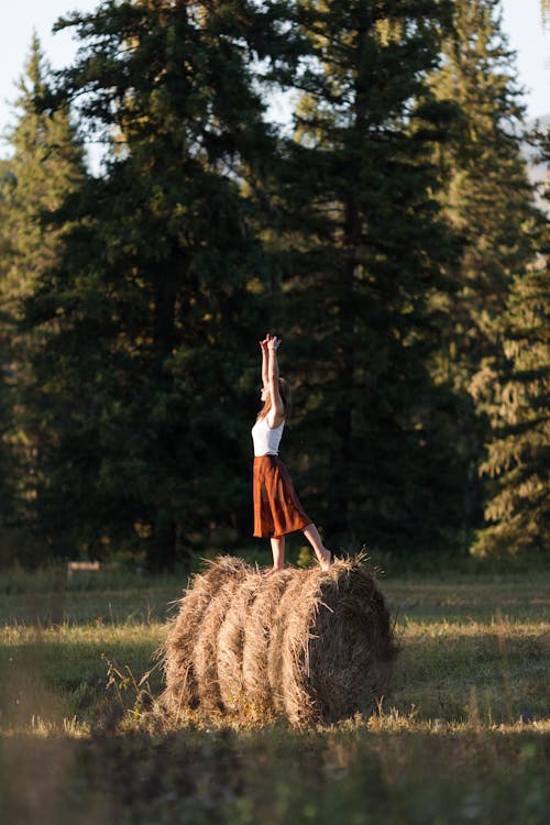 Woman Standing on Straw Bale with Raised Arms