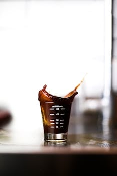 High-speed capture of coffee splashing in a measuring shot glass on a reflective surface.