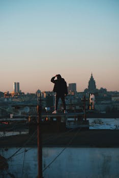 A lone man stands on a rooftop with a city skyline in the morning light, capturing a sense of exploration and solitude.