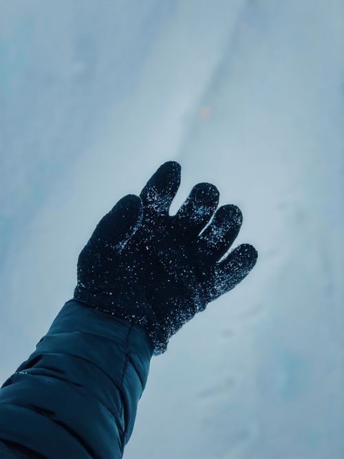 Free Close-up of a black gloved hand reaching into a snowy winter landscape, showcasing cold weather attire. Stock Photo