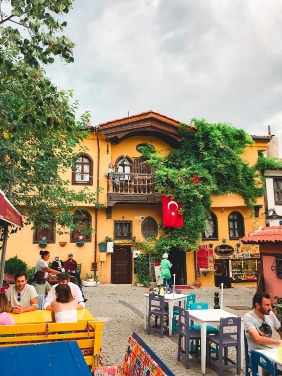 Free A vibrant outdoor cafe in Turkey with people dining under a cloudy sky, featuring a Turkish flag. Stock Photo