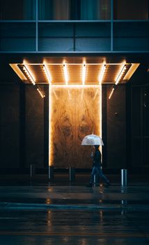 Person walking with an umbrella on a rainy evening in Minneapolis, showcasing modern architecture.