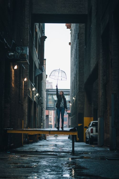 Free Young woman poses with umbrella in a dramatic urban alley setting. Stock Photo