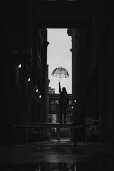 A silhouette holding an umbrella stands in a dimly lit alley in Minneapolis, creating a moody urban scene.