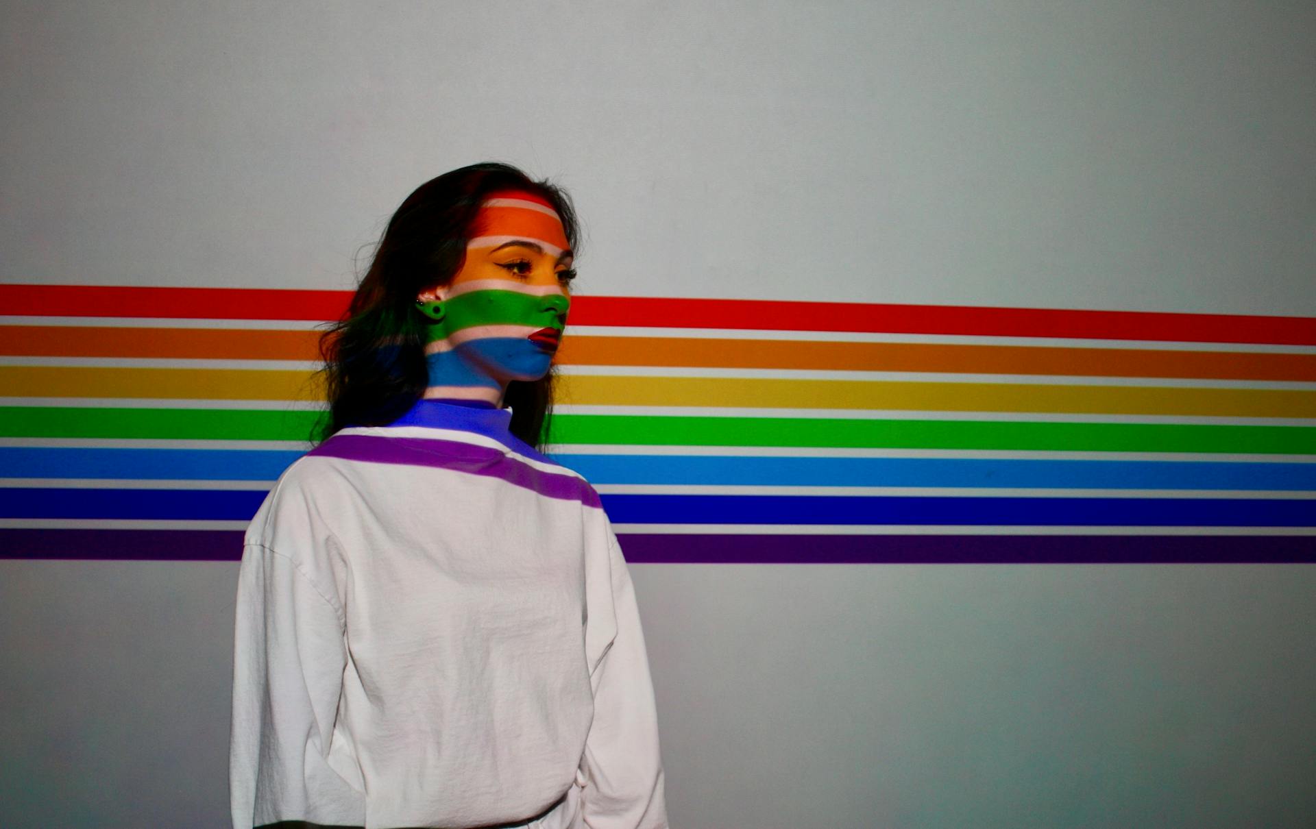 Woman in a studio with colorful rainbow light projections on her face against a neutral background.