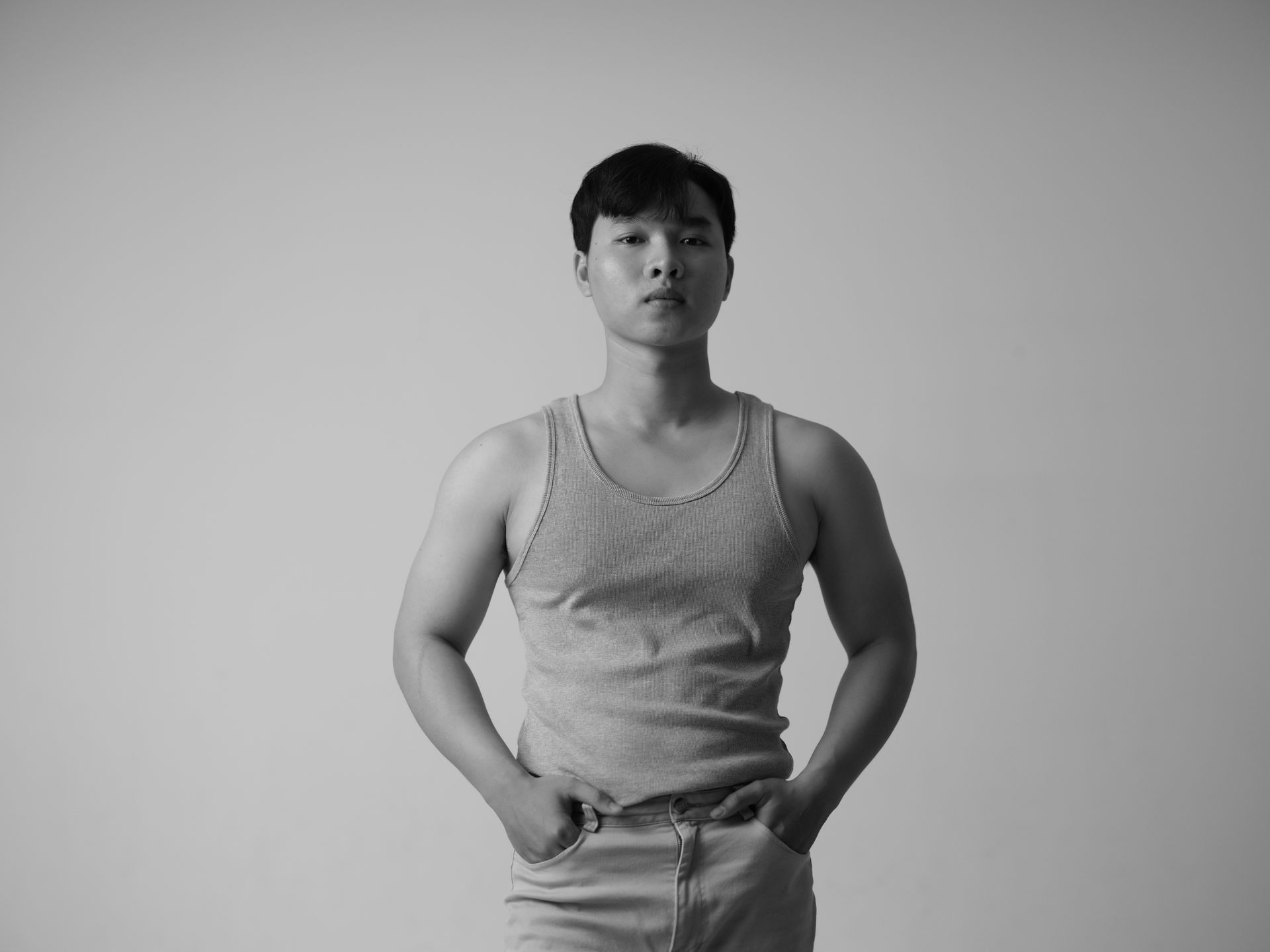 Stylish black and white portrait of an Asian man wearing a tank top in a studio setting.